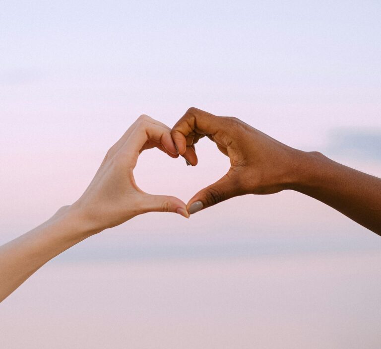 A powerful image of unity and diversity with two hands forming a heart against a serene pastel sky.